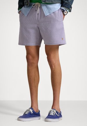 Gestreifte Shorts aus lavendelfarbenem und weißem Stoff mit Kordelzugbund, kombiniert mit blauen Stoffschuhen. Verfügt über ein kleines Logo-Detail.