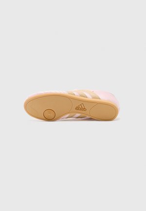 Jasnoróżowy but sportowy Adidas pokazany od spodu z beżową gumową podeszwą i logo Adidas na środku.
