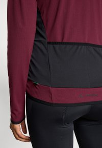 Dugi rukav sportski gornji dio s bordo gornjim dijelom i crnim donjim dijelom, teksturirana tkanina i detalj s logotipom na rubu.