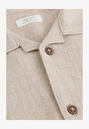 Beežist linast särk tekstuurse pinnaga, millel on krae, pruunid nööbid ja silt, millel on kiri "NEXT, VALMISTATUD BANGLADEŠIS".