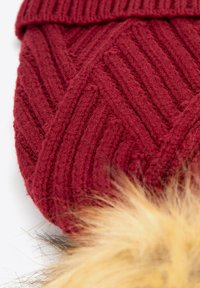 Cuffia bordeaux lavorata a maglia con motivo a zigzag testurizzato e un soffice pompon in pelliccia color sabbia sulla sommità. Materiale morbido e caldo.