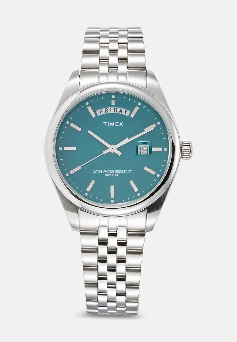 Montre Timex avec un cadran turquoise, des index argentés, un bracelet en acier inoxydable, un affichage de la date et une résistance à l'eau jusqu'à 5 ATM.