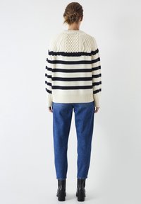 Maglione lavorato a maglia con righe orizzontali bianche e blu scuro, con un retro testurizzato e orlo a coste. Indossato con jeans blu a taglio rilassato e stivali neri.