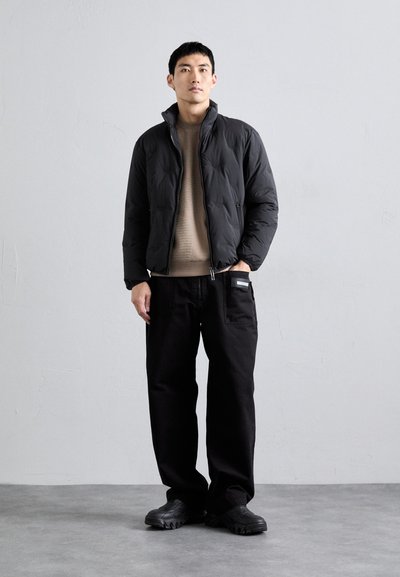 Casaco puffer preto com colarinho alto, suéter de malha bege, calças pretas largas e sapatilhas pretas. Design minimalista com bolsos.