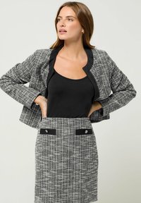 Blazer in tweed bianco e nero su misura con colletto arrotondato, abbinato a una gonna coordinata con dettagli e bottoni neri.