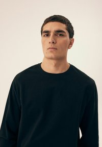 Czarna, długi rękaw, bawełniana koszulka z okrągłym dekoltem, charakteryzująca się gładką teksturą i luźnym krojem, bez widocznych wzorów czy detali metalowych.