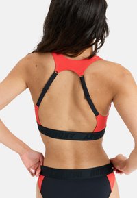 Top bikini rosso e nero con design a schiena scoperta. Caratterizzato da spalline nere regolabili e una fascia con logo lungo il fondo. Texture liscia.