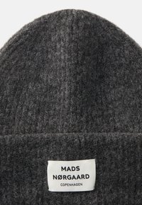 Bonnet en tricot gris avec un motif tissé texturé. Présente une étiquette blanche avec des lettres noires indiquant "MADS NØRGAARD COPENHAGUE" en bas.