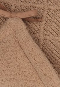Bruine gebreide stof met kabelpatronen naast zachte beige fleece stof, bijeengebonden met een bijpassende beige strik.