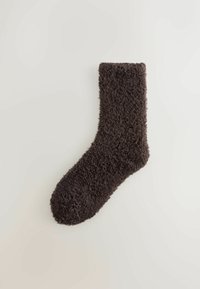 Hnedá, nadýchaná ponožka vyrobená z mäkkého materiálu. Má rebrovaný lem, okrúhly prst a štruktúrovaný povrch. Je strednej dĺžky, do polovice lýtka.