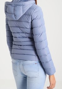 Ljusblå pufferjacka med huva, som har kviltade horisontella sektioner. Mjuk textur, åtsittande design och elastiska ärmslut.