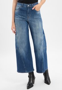 Wide-leg blue denim jeans with a faded finish, front pockets, and contrasting stitching. Paired with black ankle boots.