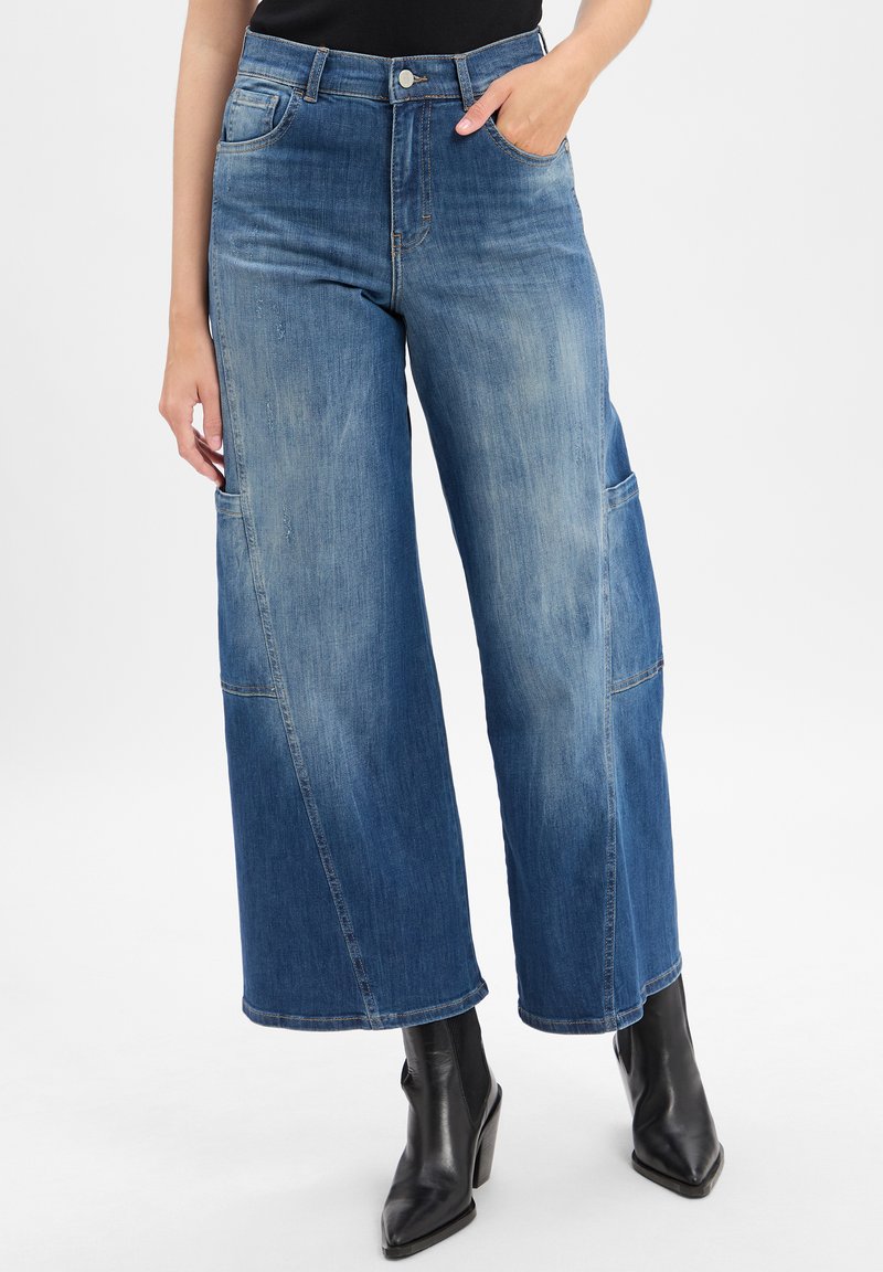 Wide-leg blue denim jeans with a faded finish, front pockets, and contrasting stitching. Paired with black ankle boots.