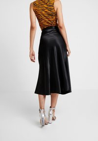 Schwarze Satin-Midi-Rock mit fließendem Design, kombiniert mit metallischen silbernen High-Heels. Das Oberteil zeigt ein auffälliges orange-schwarzes Muster.