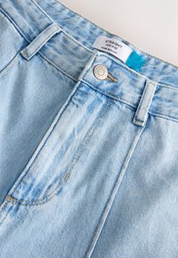 Jeans dritti a vita alta in denim blu chiaro con dettagli sbiaditi. Presentano cuciture decorative, chiusura frontale con bottoni e un'etichetta interna.