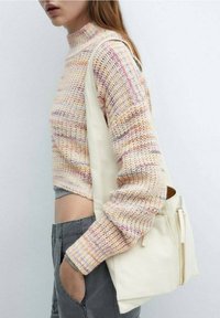 Maglione lavorato a maglia in tonalità pastello con collo alto, abbinato a una borsa color crema chiaro. Il maglione presenta un taglio corto e un motivo texture.
