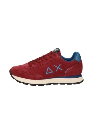Sneaker in suede rosso con interno blu, suola bianca, suola esterna nera e simboli blu a forma di triangolo e croce sul lato.
