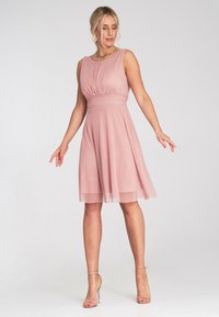 Różowa sukienka z dopasowaną górą, plisowanymi detalami i rozkloszowanym dołem. Wykonana z lekkiego materiału z przezroczystą warstwą.