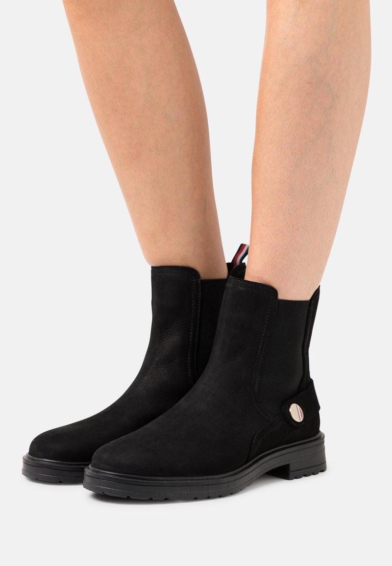 Bottines noires en daim, avec un panneau élastique sur le côté, un bout rond et un accent circulaire en métal argenté sur le côté extérieur.