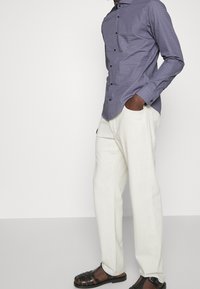 Overhemd met knopen in paars met een textuurpatroon, gecombineerd met lichte witte broeken en zwarte geweven sandalen.