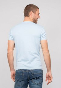 T-shirt bleu clair à manches courtes en tissu doux, design ajusté, texture lisse, porté avec un jean en denim foncé présentant des coutures au niveau des poches arrière.