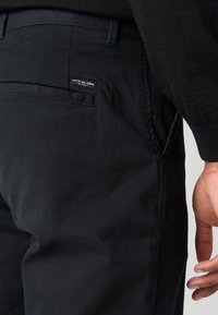 Pantalons en coton noirs avec une texture lisse, dotés d'une poche arrière avec une étiquette. Coupés avec une coupe droite et des poches latérales.