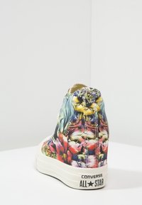 Hooggesneden Converse schoenen met een bloemenstofontwerp, multicolore bloemen op canvas, witte rubberen zool en zwart logo op de hak.