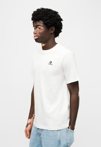 Λευκό βαμβακερό T-shirt με κοντά μανίκια και στρογγυλή λαιμόκοψη. Διαθέτει μαύρο λογό τυπο Converse στο αριστερό στήθος. Φοριέται με ανοιχτόχρωμο τζιν.