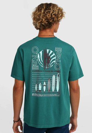 Turkooise katoenen T-shirt met een grafische print van surfplanken en een surfer op de achterkant, met witte en zwarte details. Korte mouwen, losse pasvorm.