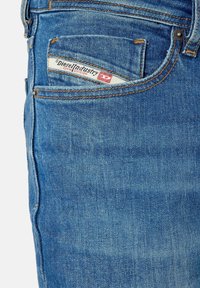 Jeans de mezclilla azul con un diseño clásico de cinco bolsillos, costuras cosidas y una etiqueta de marca visible en el bolsillo de la cadera.