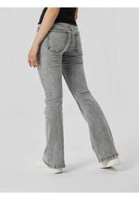 Jeans grigi con gamba svasata e finitura in denim texturizzato, dotati di tasche posteriori e vita aderente, abbinati a sneakers bianche.