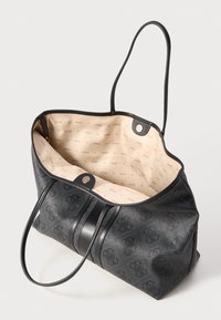Grote zwarte strandtas met een gestructureerde buitenkant en gladde leren accenten. Beige binnenkant met een herhalend "GUESS" logo patroon. Lange hengsels.