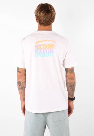 T-shirt en coton blanc avec un graphique textuel coloré "OXBOW" au dos. Manches courtes, col rond et coupe décontractée.