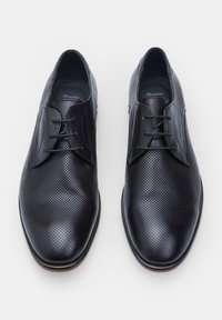 Scarpe in pelle nera con design perforato, texture liscia, chiusura con lacci e punta tondeggiante. Suola in gomma con leggera lucentezza.