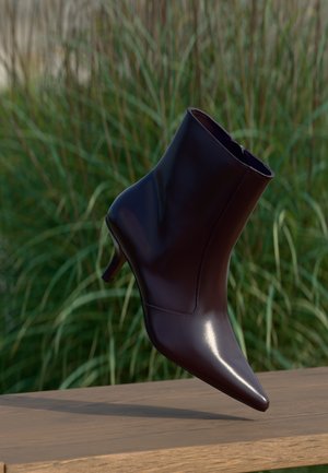 Bota de tobillo de cuero negro brillante con punta afilada y tacón de gatito sobre una superficie de madera, con un fondo de hierba verde.
