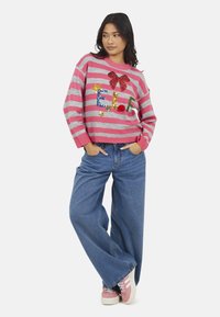 Pull en tricot rayé rose et gris avec un nœud en sequins et le texte "E.L.F.", associé à un jean en denim bleu ample et des baskets roses avec des rayures blanches.