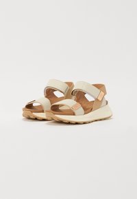 Beige sandaler med teksturert overdel, to justerbare stropper og en polstret såle. Gummiyttersåle med et mønstret grep for bedre feste.