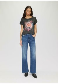 T-shirt noir à manches courtes avec un design graphique floral, associé à un jean large bleu clair et des bottes à talons noires.