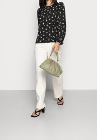 Blusa nera a fiori con maniche a sbuffo, pantaloni crema e borsa a tracolla in ecopelle verde con design arricciato e manici corti. Sandali neri con tacco.