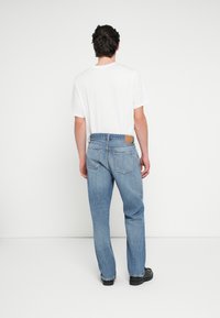 Μπλε τζιν παντελόνι με κανονική ίσια γραμμή, δύο πίσω τσέπες και καφέ δερμάτινο ταμπελάκι στη μέση, συνδυασμένο με απλή λευκή μπλούζα.