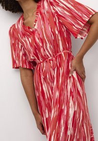 Robe rouge et rose à motif avec manches courtes, devant boutonné et ceinture nouée à la taille. Tissu fluide avec un design texturé strié.