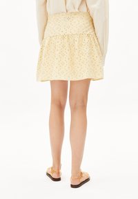 Jupe jaune avec broderie florale, taille ajustée et ourlet évasé. Assortie à des sandales nudes, mettant en valeur un design de tissu texturé.