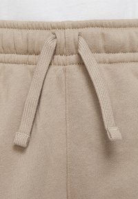 Béžové tepláky s texturovaným elastickým pasem se stahovacími šňůrkami, vyrobené z měkké látky, kladoucí důraz na pohodlí a volný střih.