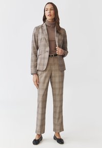 Hnědý kostkovaný blazer s přiléhavým střihem, spárovaný s hnědým rolákem a odpovídajícími kostkovanými kalhotami, doplněný černými balerínami.