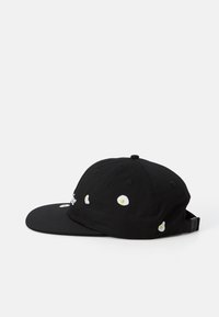 Black baseball cap made of cotton with a flat brim, featuring white embroidered egg accents and a snapback closure at the rear.