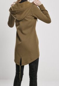 Olivově zelená mikina z měkké tkaniny, s asymetrickým zakončením, klokaní kapsou a nastavitelnou šňůrkou na zádech.