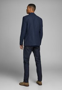 Blazer blu navy realizzato in tessuto testurizzato, con uno spacco singolo e polsini con bottoni, abbinato a jeans di denim scuro e stivali marrone chiaro.