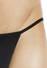 Schwarze Tanga-Bademode mit dünnen Trägern, glatter Textur und minimaler Abdeckung, die den Hautton und subtile Körperhaare zeigt.