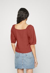 Rostfarbende Bluse mit Puffärmeln und quadratischem Ausschnitt, kombiniert mit einem hellblauen Jeansrock mit fransigem Saum.