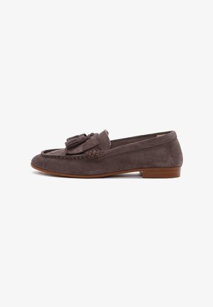 Mocassin en daim gris avec un petit talon, présentant des détails de glands sur le devant et des surpiqûres décoratives sur les bords. Texture lisse sur l'ensemble.